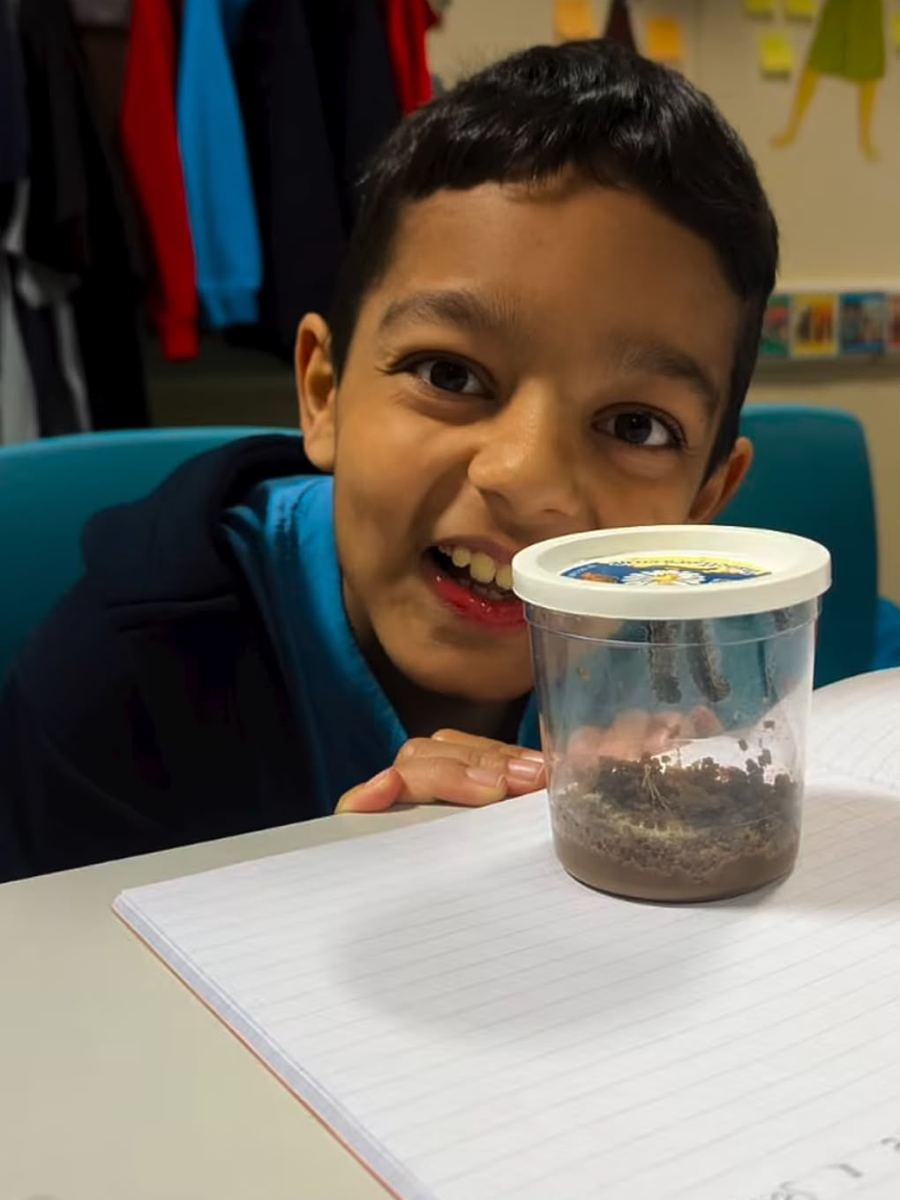 A learner grinning next to a minibeast pot on his desk